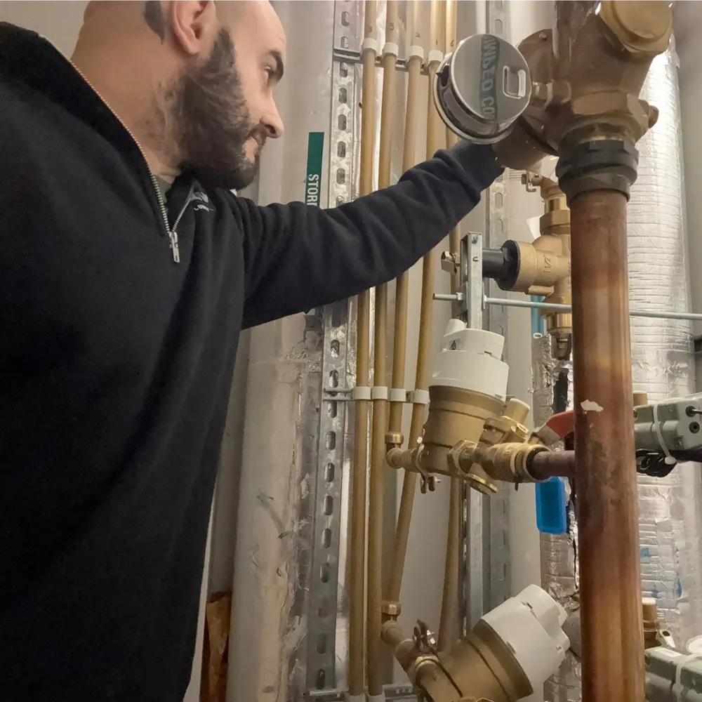 Controlled Flow Plumbing technician quality-checking hydraulic pipework and a water meter on a commercial construction site