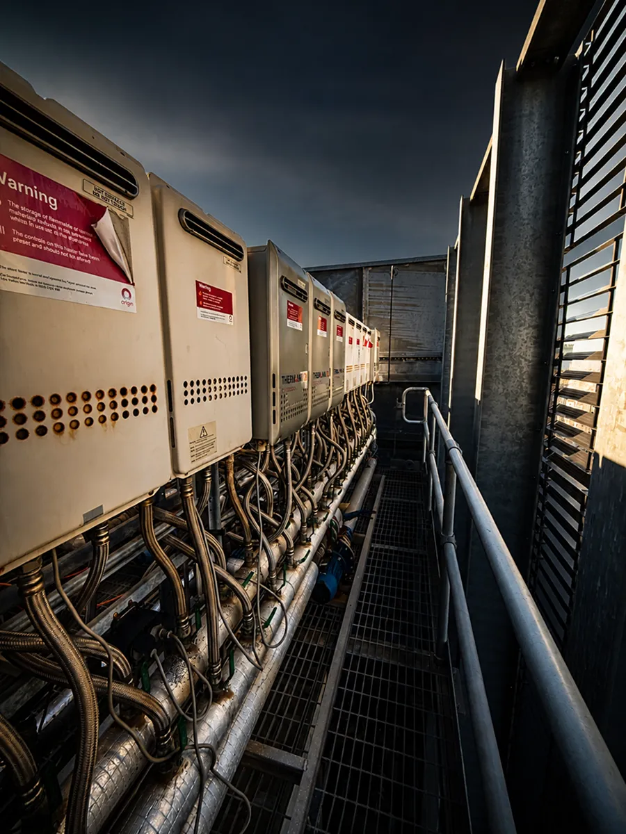 Row of gas hot water units and pipework serviced on a commercial rooftop plant deck