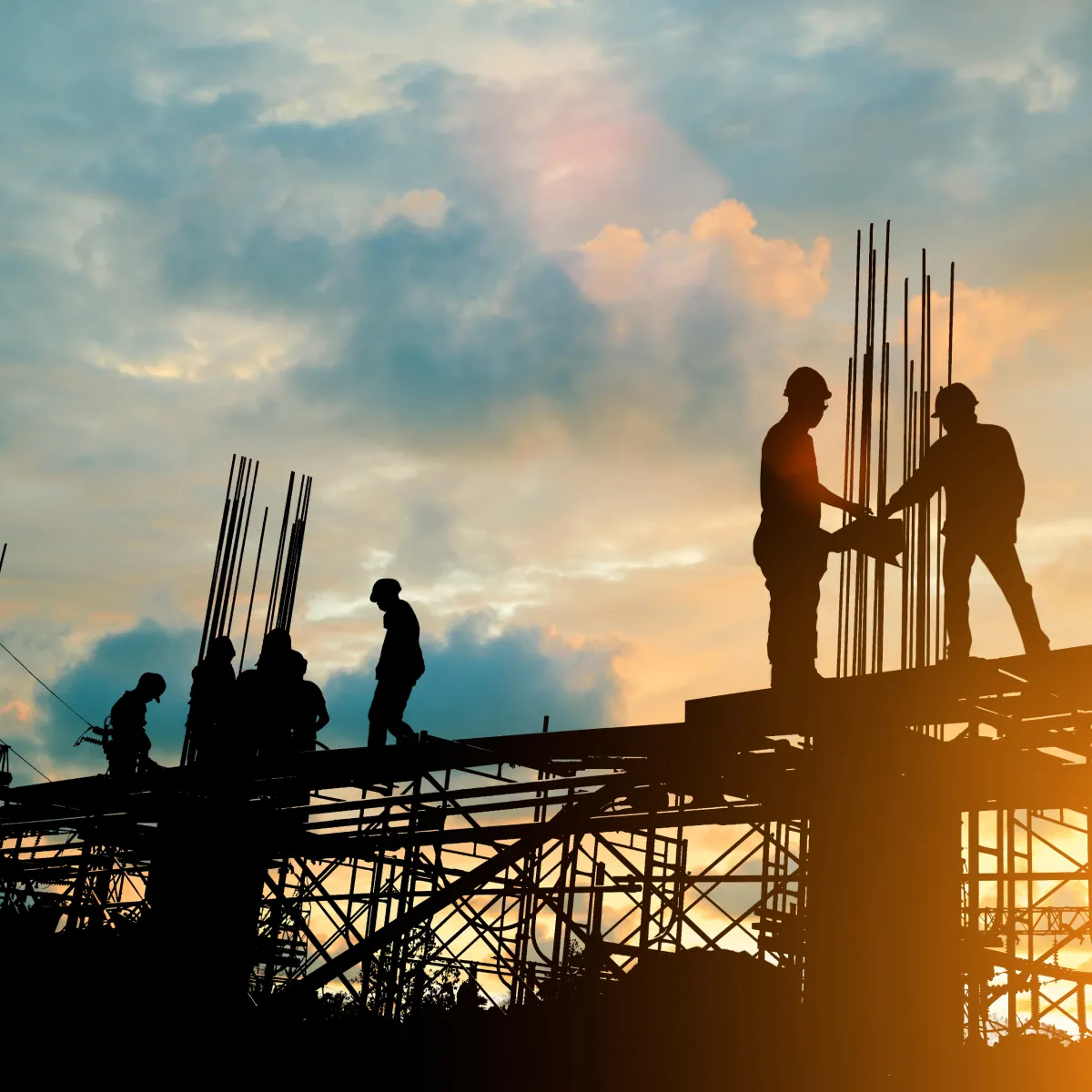 Silhouetted construction workers on scaffolding at a commercial building site at sunset